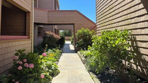 A narrow pathway flanked by buildings with wooden siding and brick walls, leading to a covered area. - Brigantine Breeze 2-BR Coastal Retreat Steps to Beach (Brigantine)