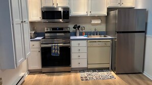 A modern kitchen with white cabinets, stainless steel appliances, and a wooden floor. - Brigantine Breeze 2-BR Coastal Retreat Steps to Beach (Brigantine)