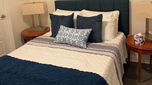 A bedroom with a bed, two bedside tables, a nightstand, a painting on the wall, and a window. - Radiant and Cozy (Memphis)