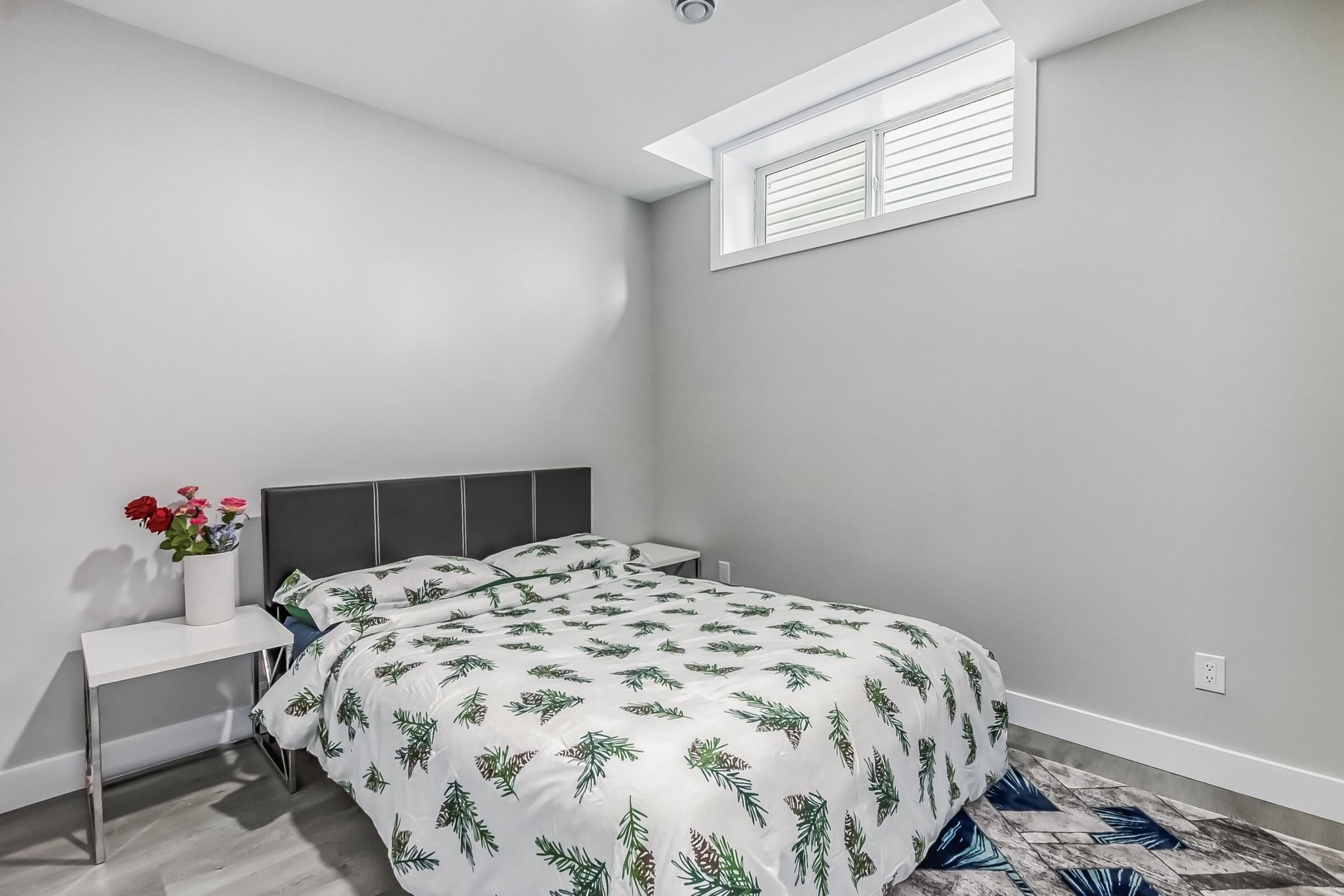 Une chambre à coucher avec un lit, une table de chevet, une commode, une fenêtre et une petite plante.