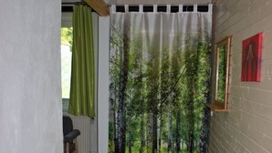 Ett rum med en gardin som föreställer en skogsmiljö, ett element, en stol och en vägg med en inramad tavla.