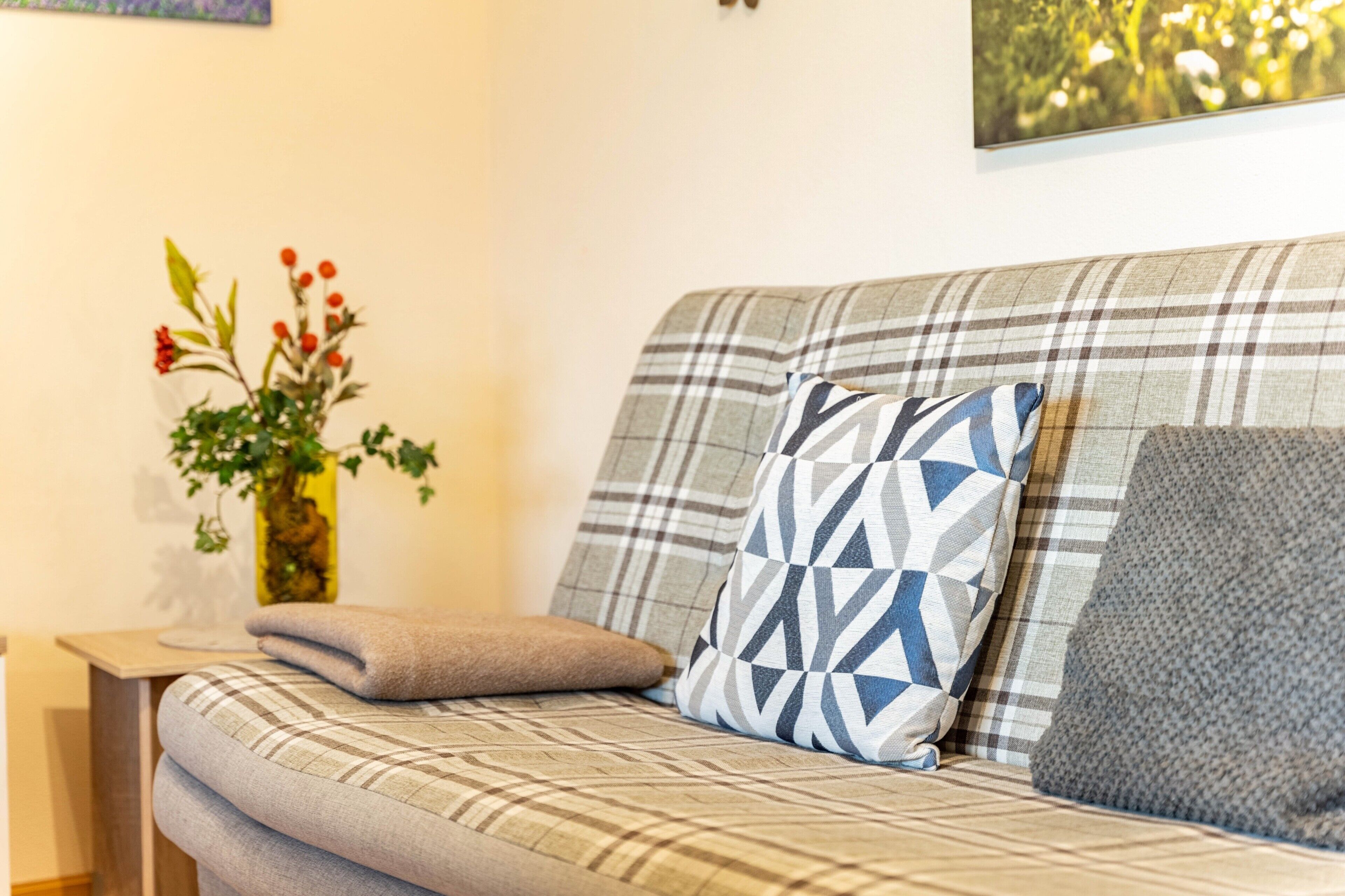 Un sofá con estampado escocés, una almohada geométrica y una almohada texturizada.