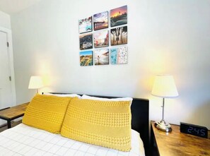 Ett hotellrum med en säng, två sänglampor, en digital klocka och en vägg med flera fotografier.