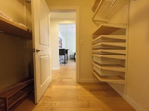 A hallway with a wooden floor, a white door, and a shelving unit on the right.