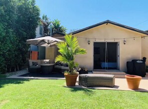 A residential backyard with a patio, outdoor furniture, a potted plant, and a sliding glass door leading to a covered area. - Big Master Suite with private entry and shared yard in Culver City (Culver City)