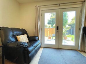 A room with a black leather sofa, a patterned pillow, and a sliding glass door leading to an outdoor area with potted plants. - Big Master Suite with private entry and shared yard in Culver City (Culver City)