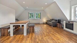 Een modern loft appartement met een eetgedeelte, zitplaatsen, een keuken en een groot raam met uitzicht op groen.