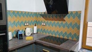 Una cocina con salpicadero de estilo geométrico en tonos verde azulado y amarillo, una estufa, un hervidor y una cafetera.