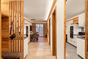 A modern kitchen with white cabinets, a dining area with a table and chairs, and a wooden partition with a bench. - Apartment 'Panorama Chalets Am Pass Thurn' with Mountain View, Private Terrace and Wi-Fi (Mittersill)