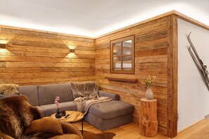 A cozy corner with a grey sofa, a wooden accent wall, a small wooden stool with a vase, and a framed picture. - Apartment 'Panorama Chalets Am Pass Thurn' with Mountain View, Private Terrace and Wi-Fi (Mittersill)