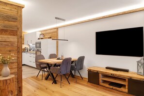 A modern kitchen with wooden accents, a dining area with a wooden table and chairs, and a mounted flat-screen TV. - Apartment 'Panorama Chalets Am Pass Thurn' with Mountain View, Private Terrace and Wi-Fi (Mittersill)