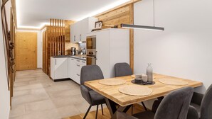 A modern kitchen with white cabinets, a wooden accent wall, and a dining area with a wooden table and grey chairs. - Apartment 'Panorama Chalets Am Pass Thurn' with Mountain View, Private Terrace and Wi-Fi (Mittersill)