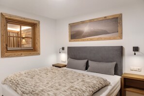 A bedroom with a bed, a window, a wall-mounted picture, bedside lamps, and a nightstand. - Apartment 'Panorama Chalets Am Pass Thurn' with Mountain View, Private Terrace and Wi-Fi (Mittersill)