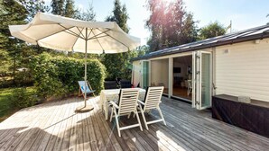 Eine Terrassenausstattung mit Tisch und Stühlen, einem großen Sonnenschirm und Blick auf ein Haus mit offener Tür.