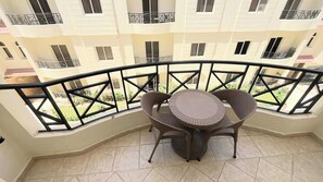 A balcony with a round table and chairs, a tiled floor, and a view of a multi-story building with balconies. - Palm Beach Piazza Beachfront lovely Apartment (Sahl Hasheesh)
