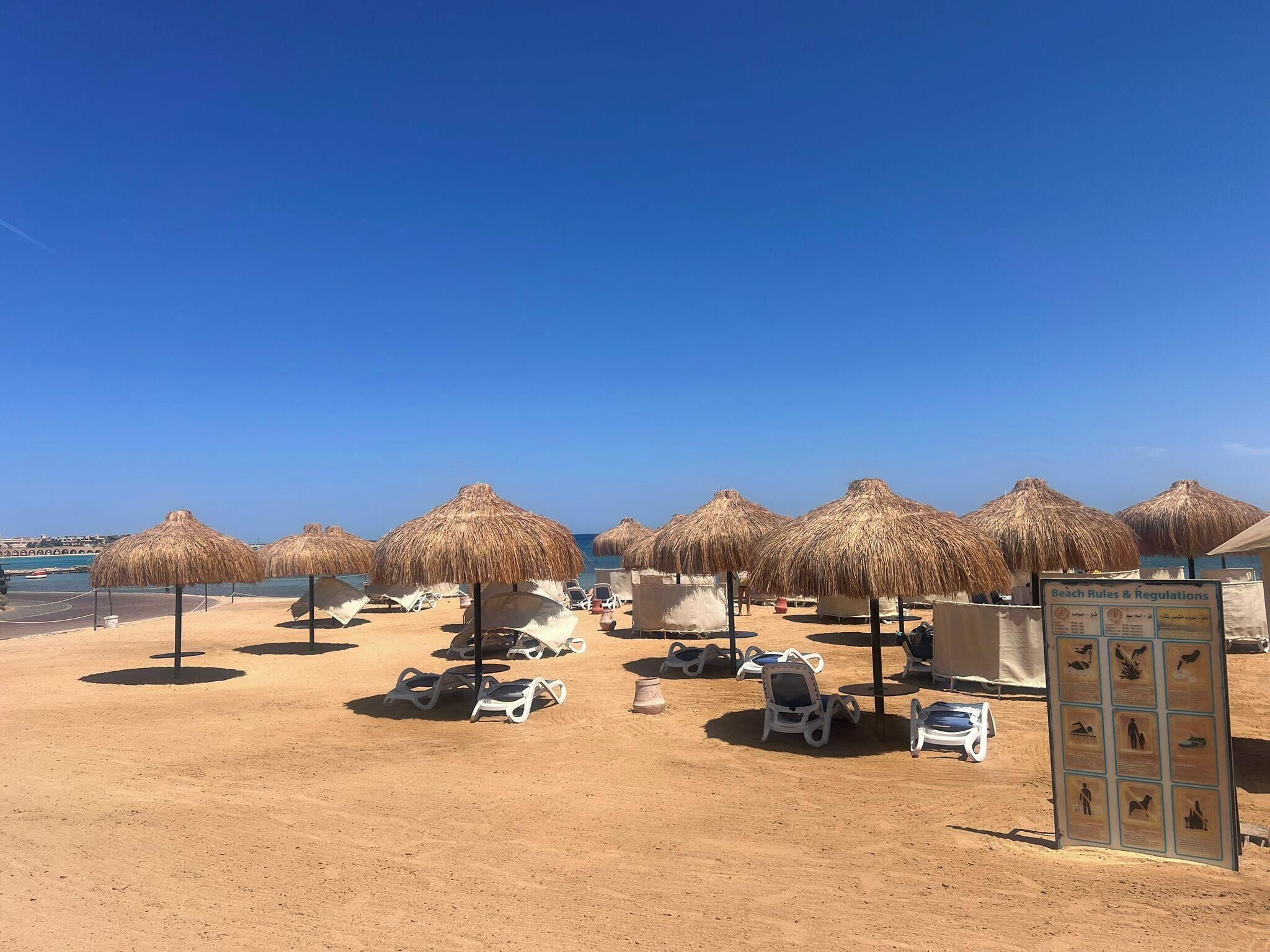 A beach with thatched umbrellas, sun loungers, and a beach rules sign.