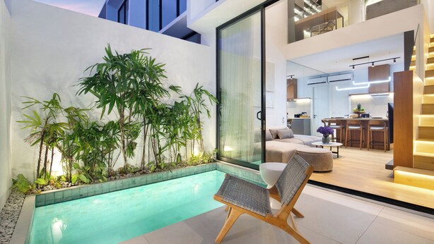 Ein moderner Poolbereich im Innenbereich mit Glaswand, Bambuspflanzen und einer Sitzecke mit Sessel und Hocker.