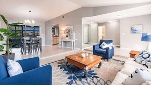 A spacious living area with a blue sofa, a wooden coffee table, and a dining area with a white table and chairs.