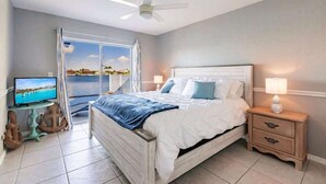 A bedroom with a bed, a TV, a nightstand, and a view of the sea.