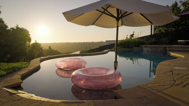 Una piscina con due cerchi gonfiabili rosa e un ombrellone grande.