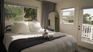 Camera da letto con un letto, cuscini, una coperta, comodino, specchio e vista sul verde.