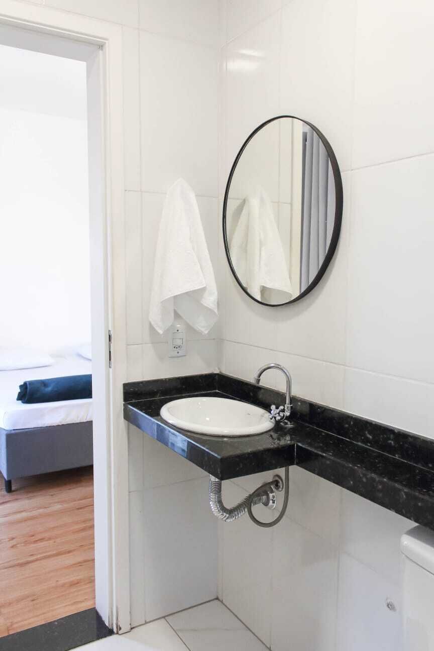 Un baño con un lavamanos blanco, una encimera negra, un espejo redondo y una toalla blanca colgada en la pared.