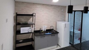 Een compacte keuken met een ingebouwde magnetron, een spoelbak en een kleine koelkast. Er is een zwart aanrecht en een houten achterwand.