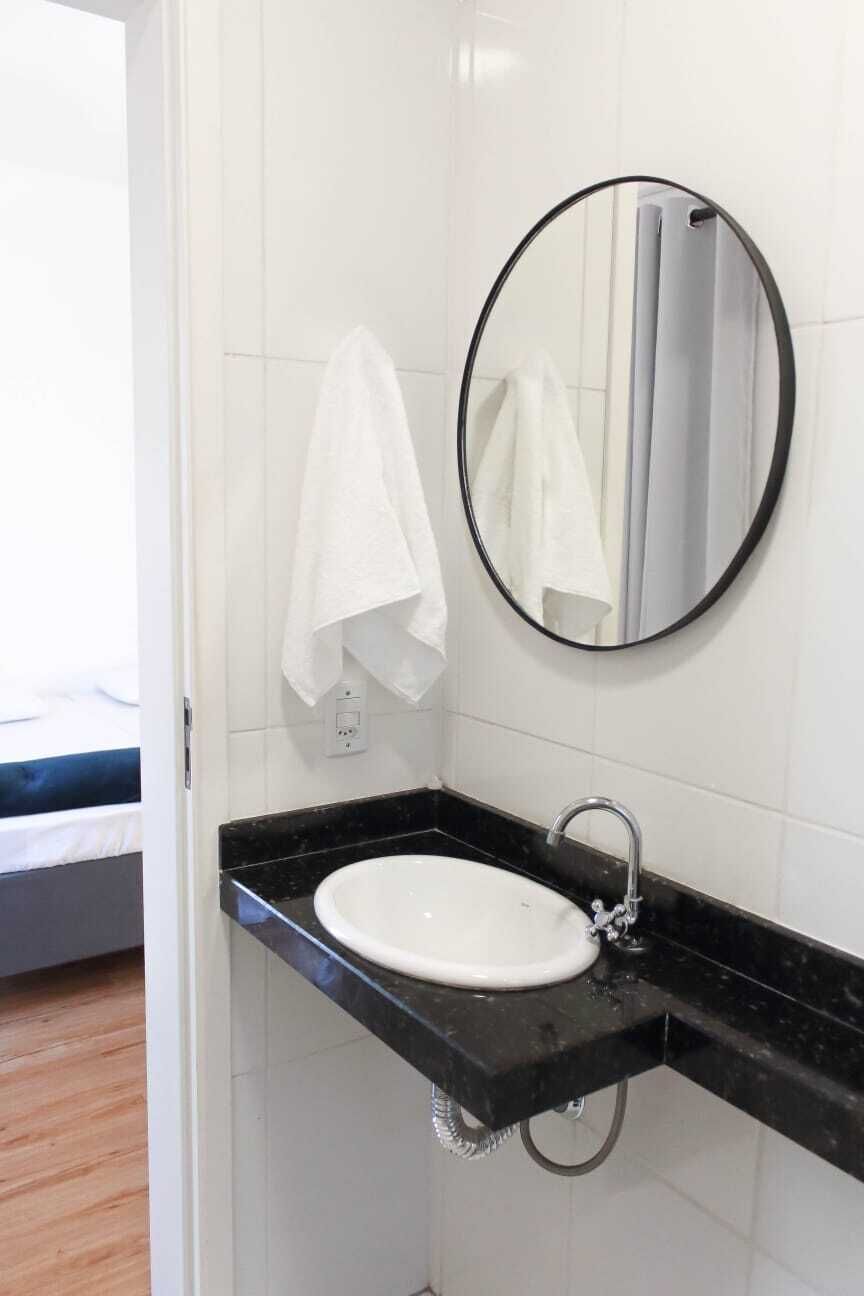 Une salle de bain avec un lavabo blanc, un plan de toilette noir et un miroir rond.