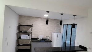 Een kleine keuken met een zwart aanrecht, een magnetron, een koelkast en een houten eettafel.