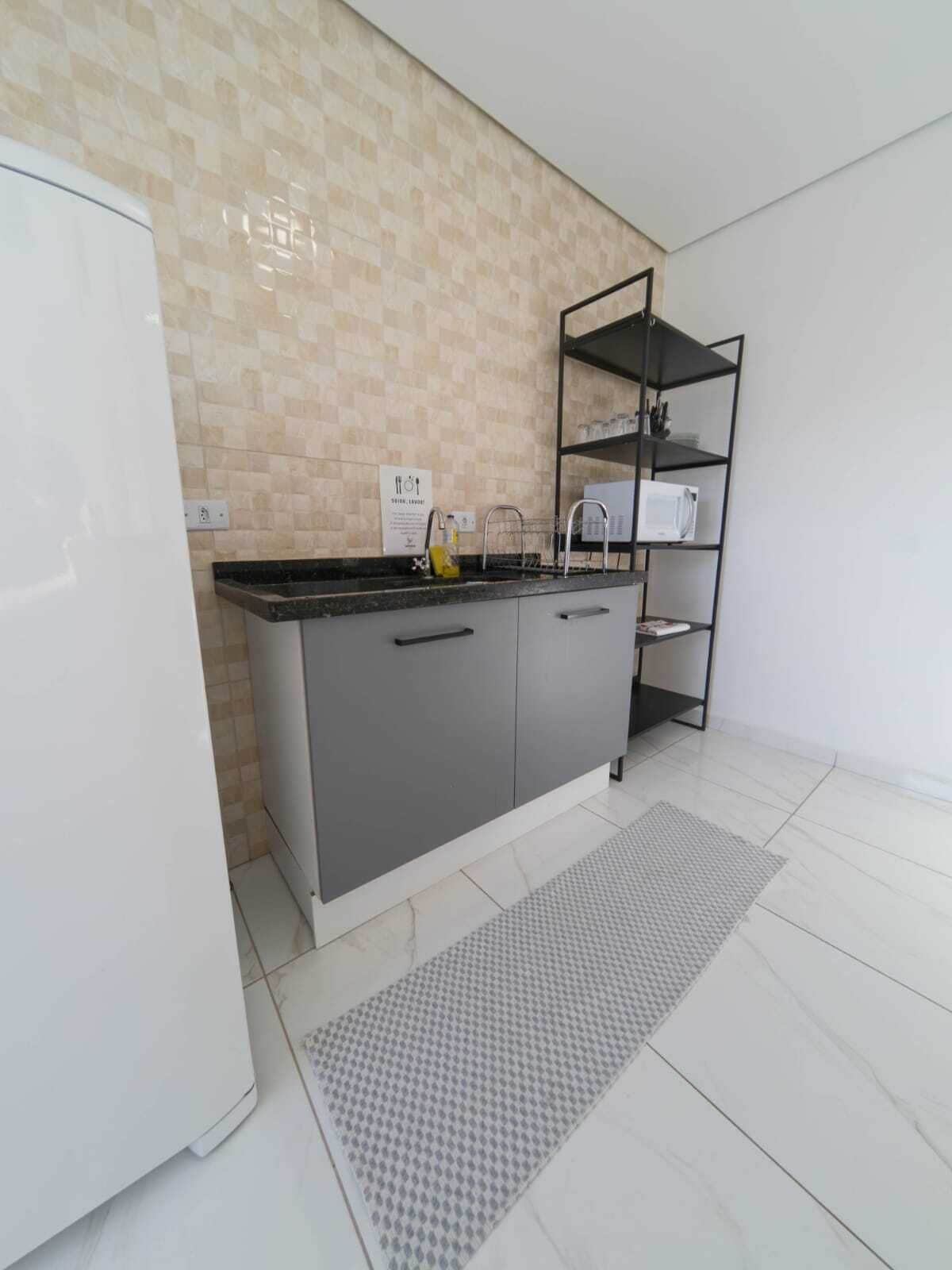 A modern kitchen with a grey countertop, a white refrigerator, a tiled backsplash, and a black metal shelf unit.