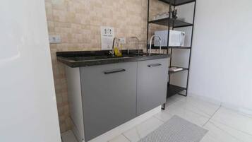 A modern kitchen with a grey countertop, a white refrigerator, a tiled backsplash, and a black metal shelf unit.