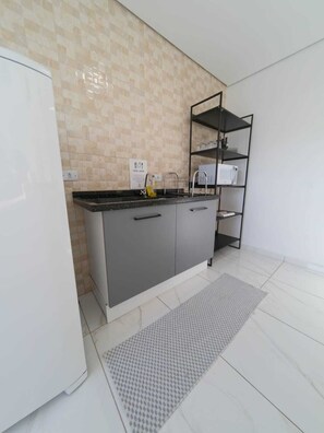 A modern kitchen with a grey countertop, a white refrigerator, a tiled backsplash, and a black metal shelf unit. - Sapucaia Flat (Santa Rita do Sapucai)