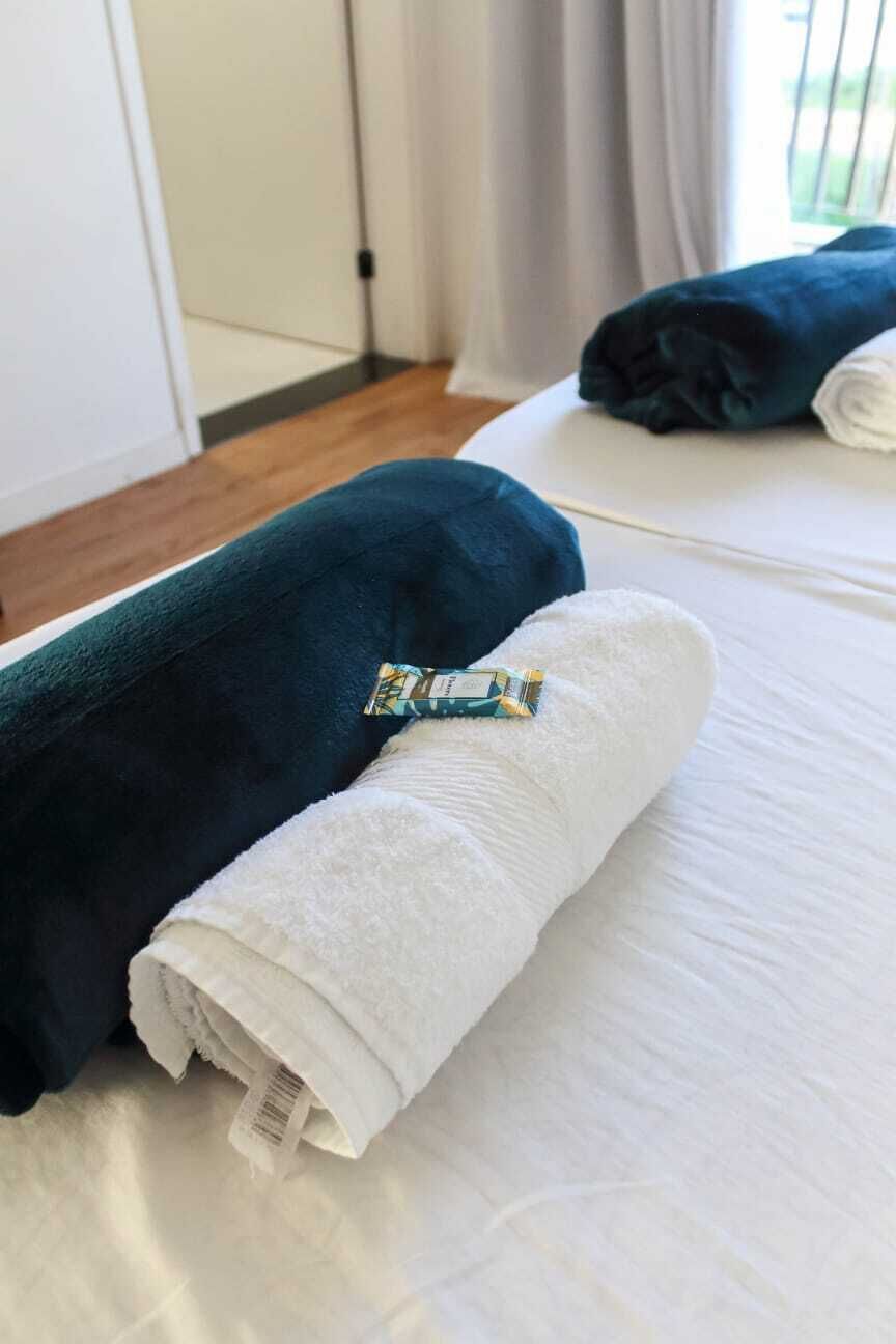 Siististi pedattu sänky, jossa on valkoinen ja tummansininen pyyhe, pieni pullo ja pyyhkeeseen kiinnitetty etiketti.