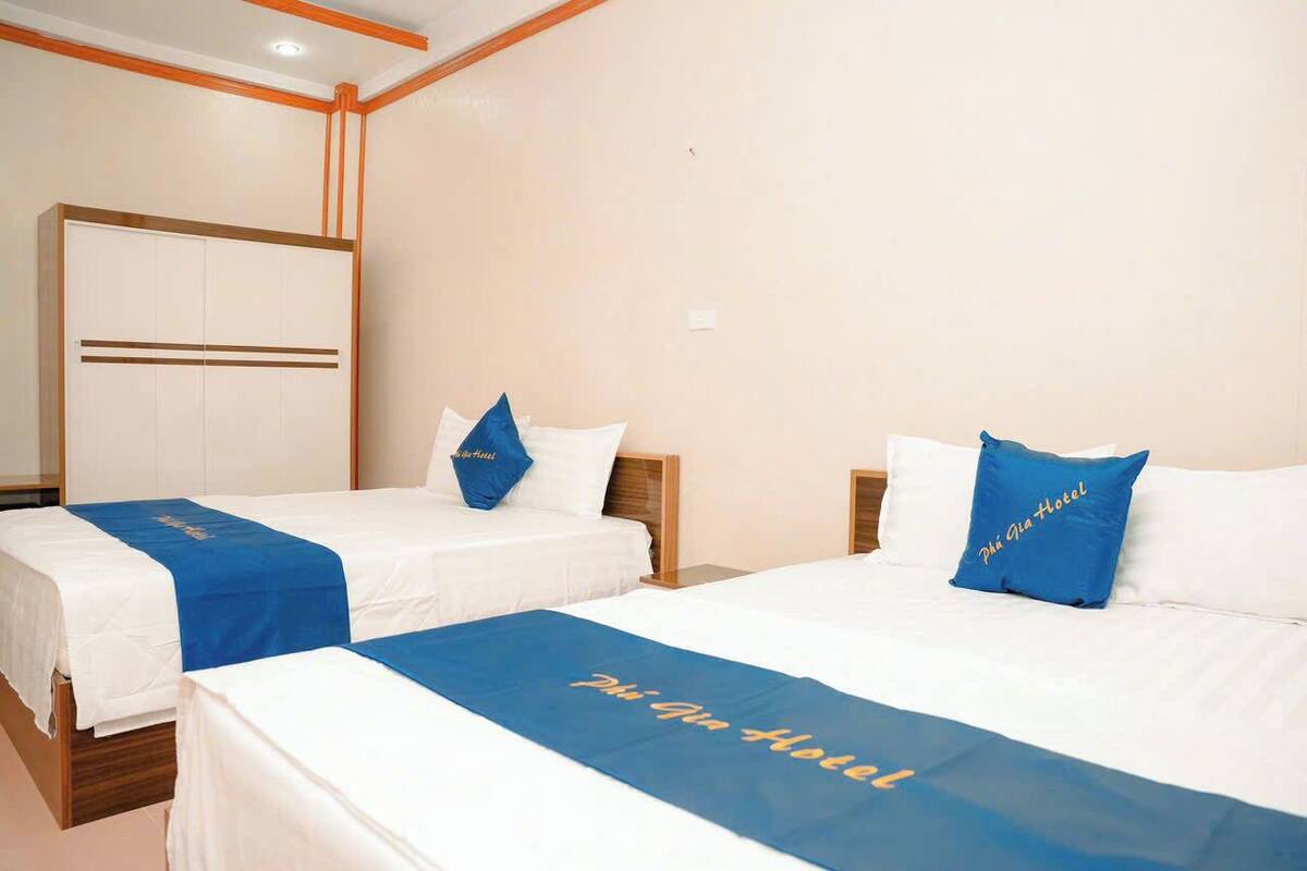 A hotel room with two beds, each with a blue bedspread and pillows, and a large wardrobe in the background.