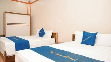 A hotel room with two beds, each with a blue bedspread and pillows, and a large wardrobe in the background.