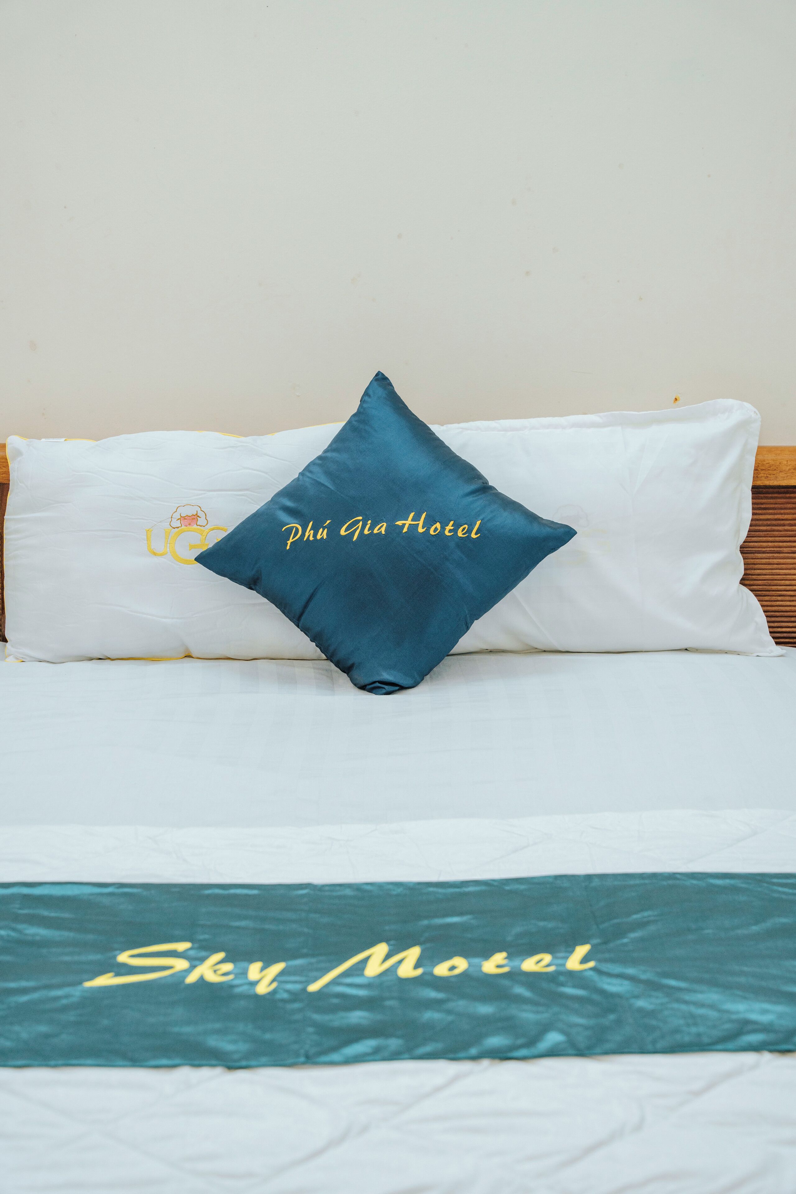Una cama con un almohadón blanco y uno azul turquesa con el texto "Phú Gia Hotel". La colcha tiene el texto "Sky Motel".