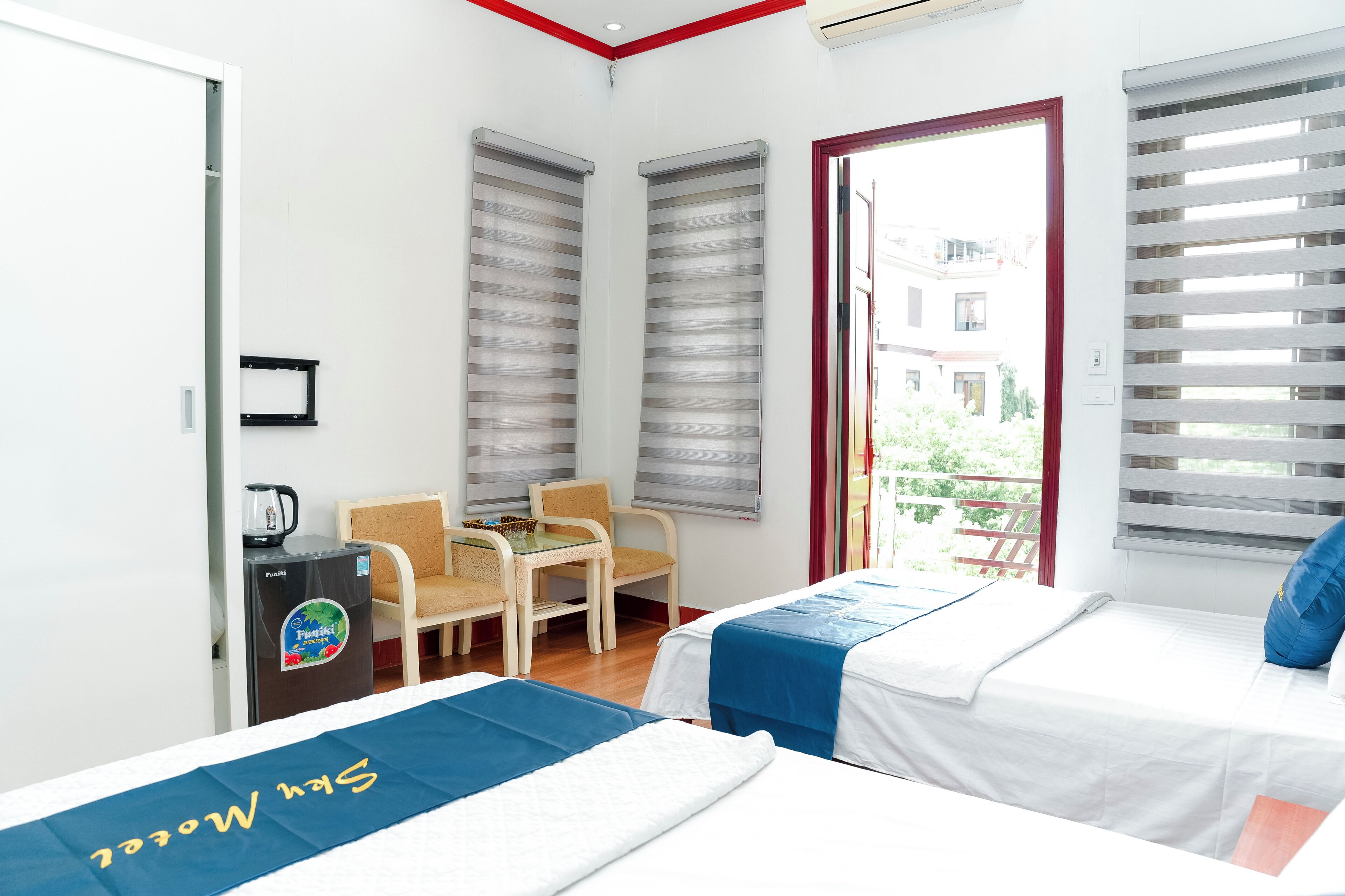 A hotel room with two beds, a small table, a chair, and a kitchenette.