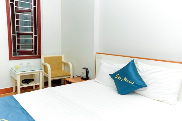 A hotel room with a bed, a chair, a small table with a kettle, and a window with a red frame. - Sky Hotel - Bac Ninh (Vo Cuong)