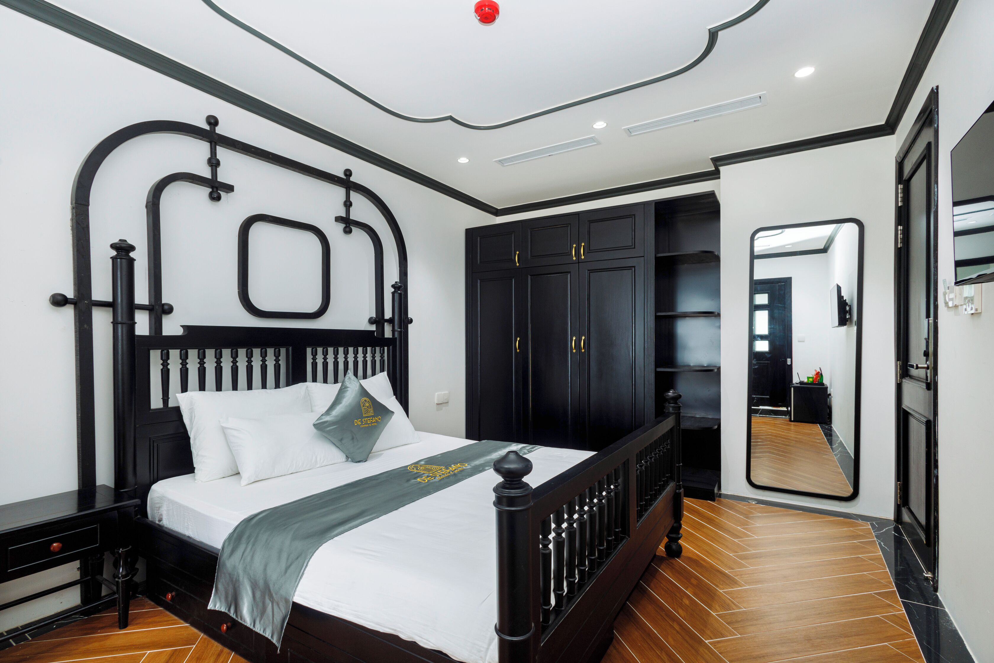 Un dormitorio moderno con un marco de cama negro, ropa de cama blanca y una manta gris.