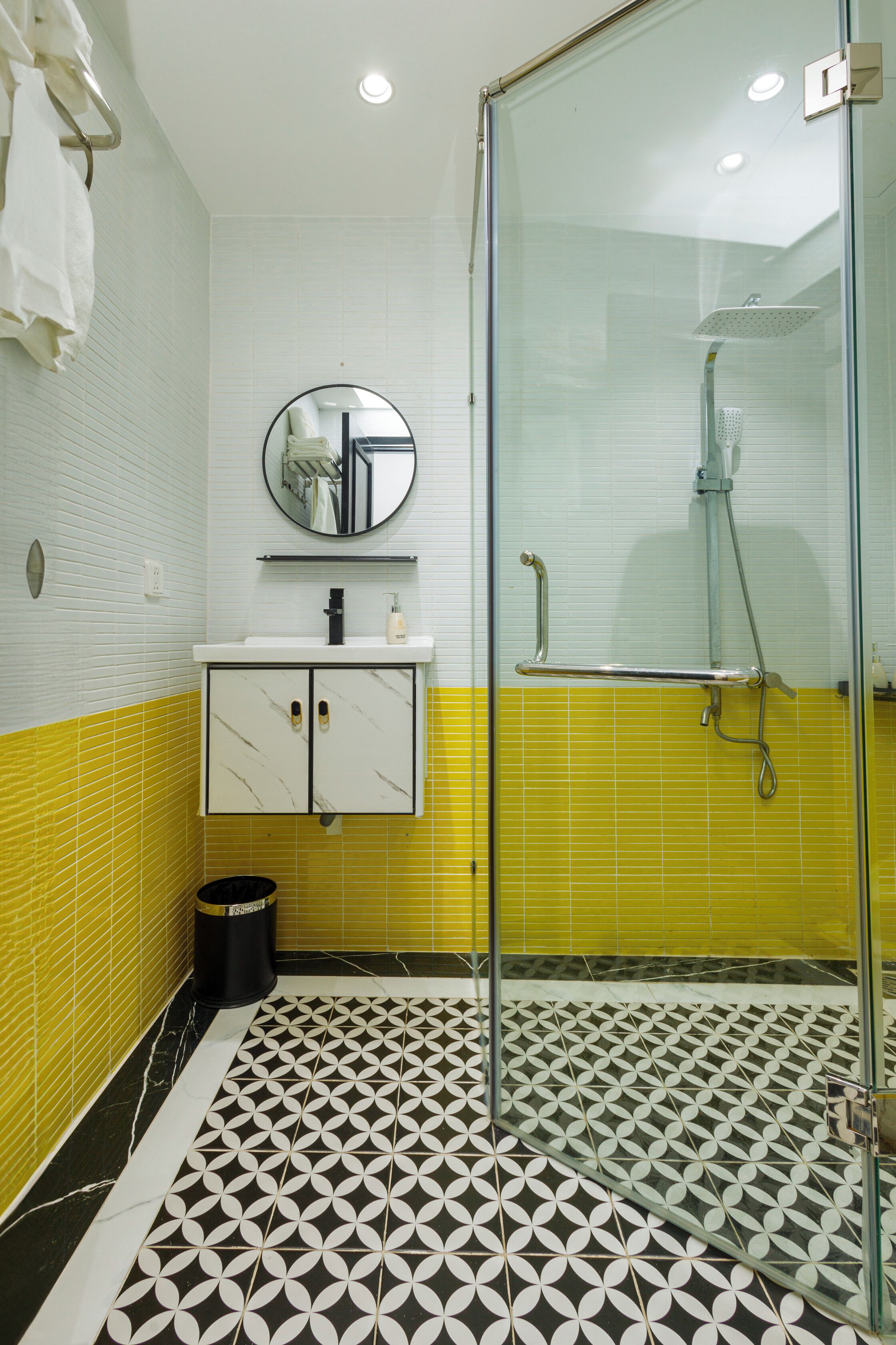 Un baño con cabina de ducha de vidrio, un lavabo con espejo y baldosas de suelo estampadas.