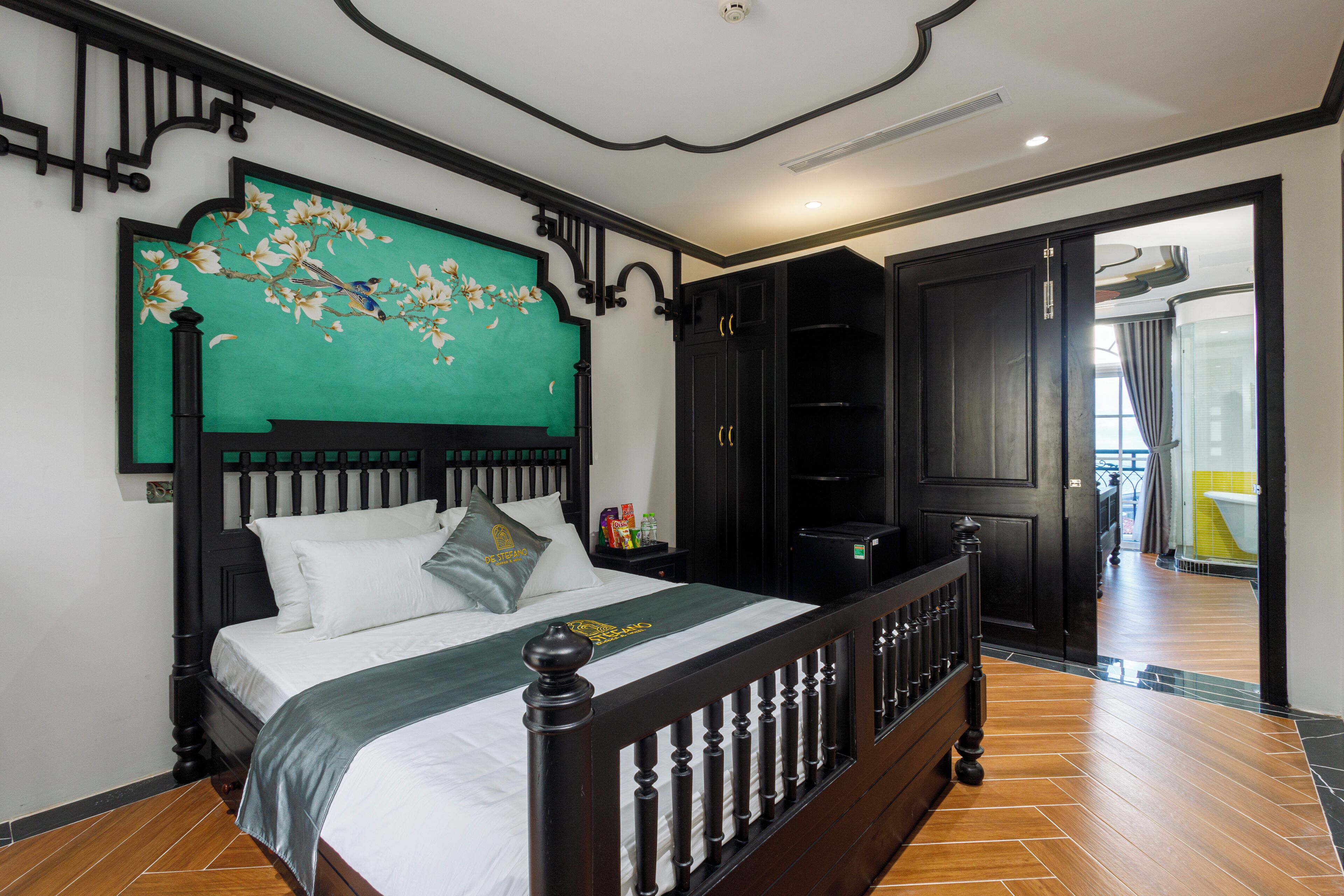 Un dormitorio con cama, cabecera de flores verdes, armario negro y suelo de madera.