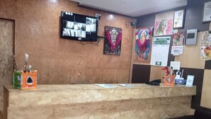 A hotel reception desk with a flat-screen TV, a calendar, and various religious posters on the wall. - Hotel Kurunji Meridian (Kodaikanal)