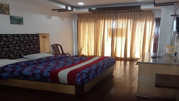 A hotel room with a large bed, a desk, and a window with curtains. - Hotel Kurunji Meridian (Kodaikanal)