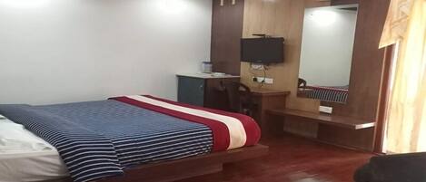 A hotel room with a bed, a desk, a chair, a television, and a mirror.