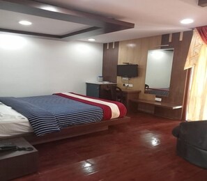 Quarto de hotel com cama, escrivaninha, cadeira, televisão e espelho.