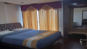 A bedroom with a bed, curtains, and a wooden floor. - Hotel Kurunji Meridian (Kodaikanal)