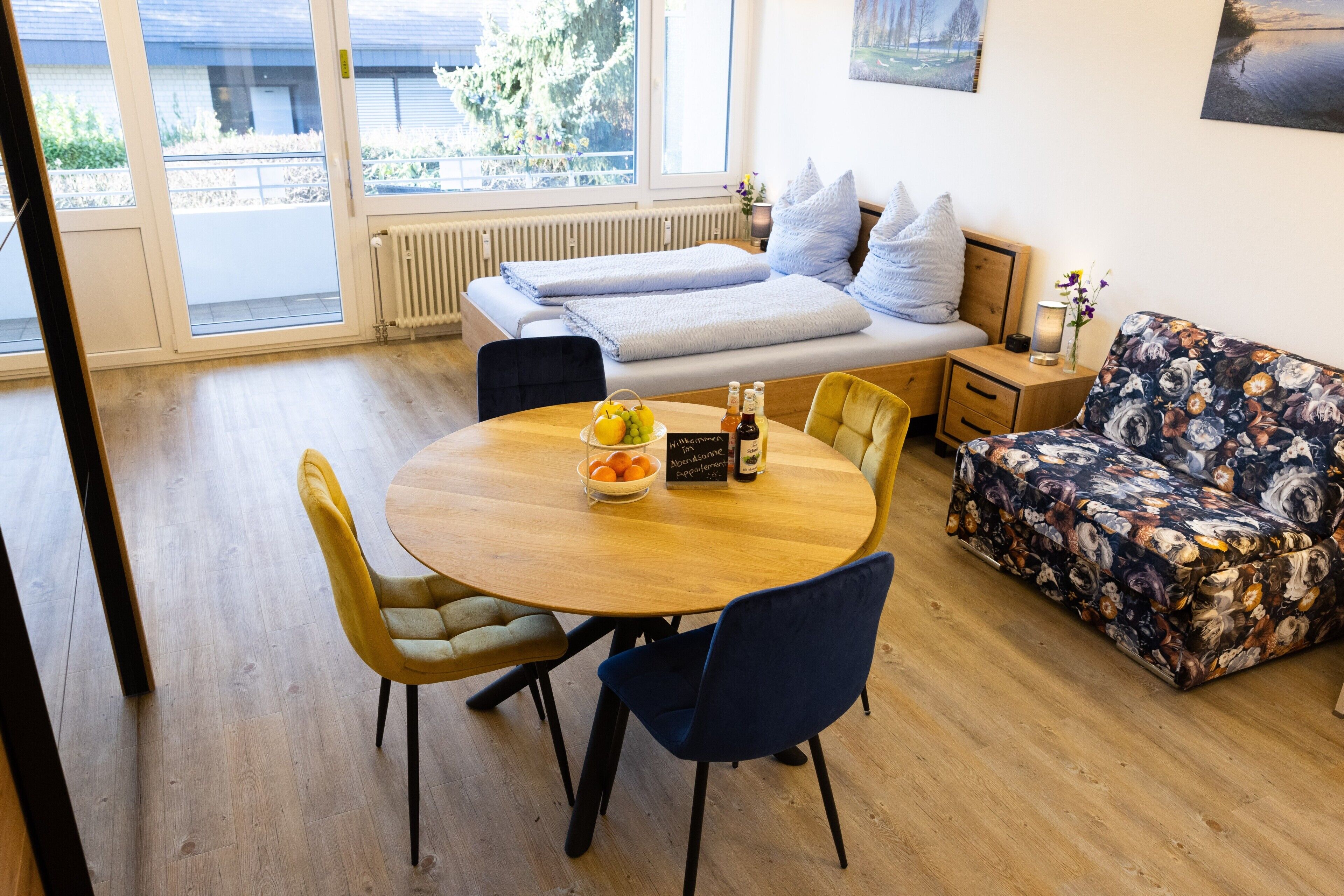 Ein Zimmer mit Bett, einer Couch, einem Esstisch mit Stühlen und einem Fenster mit Blick auf Grünflächen.