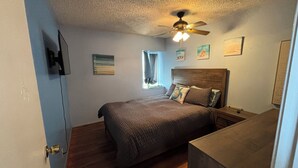 A bedroom with a bed, a ceiling fan, a window, and artwork on the walls.