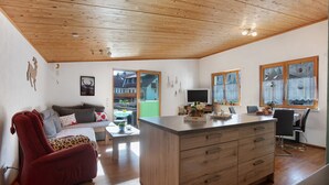 A modern interior with a wooden ceiling, a sofa, a red chair, a dining area, and a kitchen island.