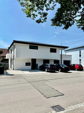 A two-story building with a flat roof, a garage, and a parking area with two cars.